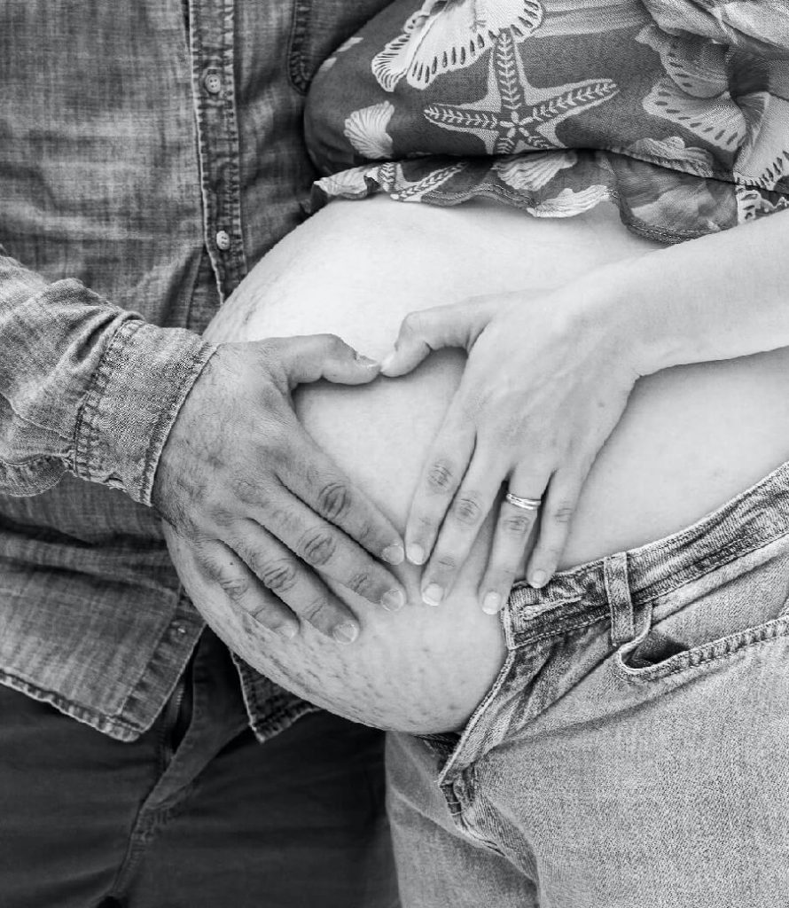 Man and woman's hands forming a heart on a pregnant stomach with stretch marks