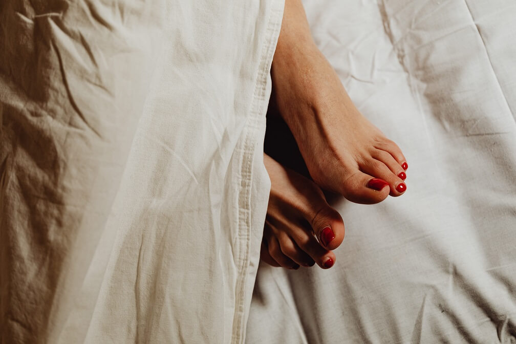 Female feet sticking out from under sheets with red nail polish on