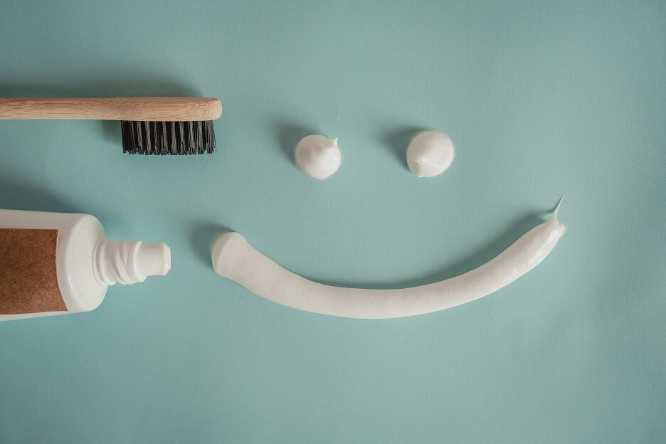 Toothbrush, opened tube of toothpaste, and a smiley face made out of toothpaste