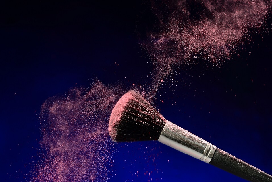 Fluffy makeup brush with makeup dust flying off of it