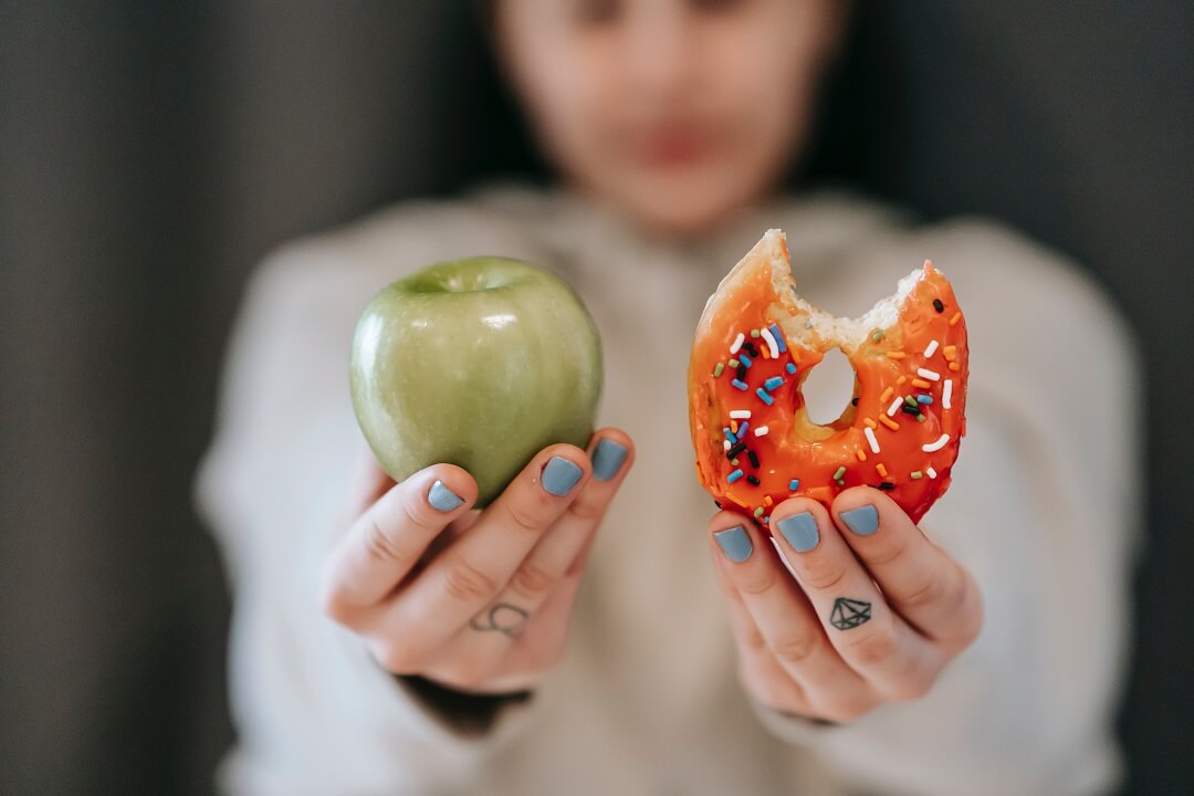 Woman holding an apple in one hand and a donut in the other