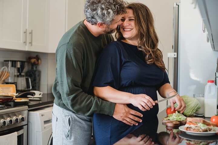 Pregnant woman making healthy meal and being embraced by her husband
