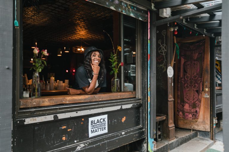 Black female business owner smiling in front of a sign that states :Black Businesses Matter"