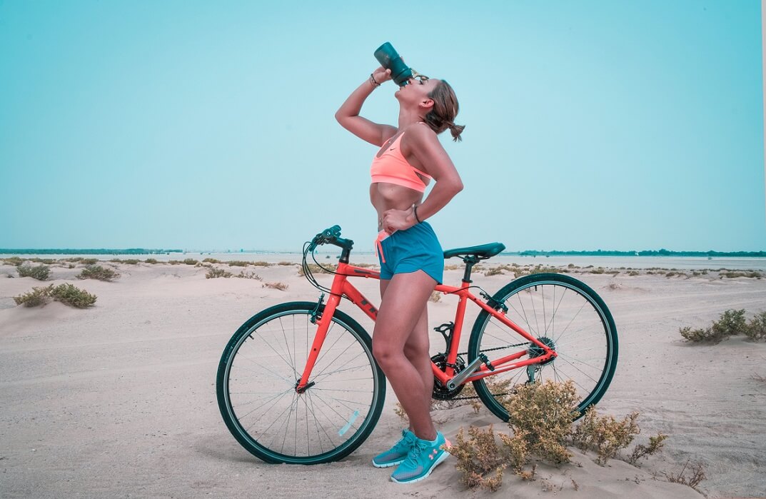 Woman in activewear standing by bike drinking from tumbler