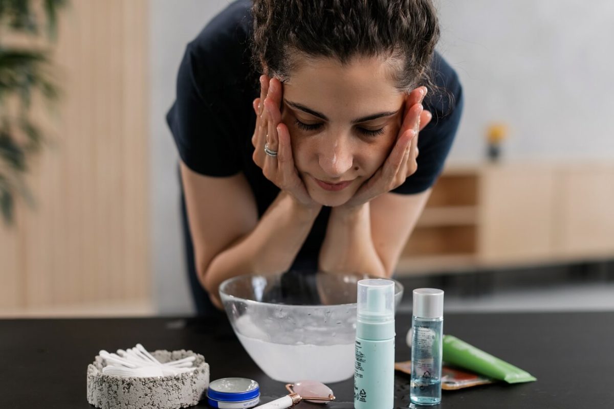 woman washing her face with exfoliator and beauty products near her