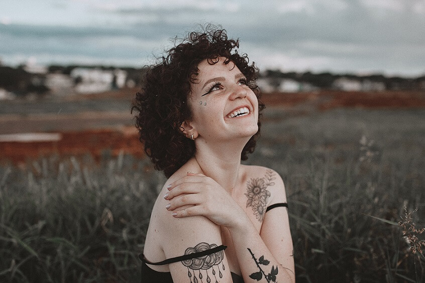Woman smiling at the sky while holding her shoulder