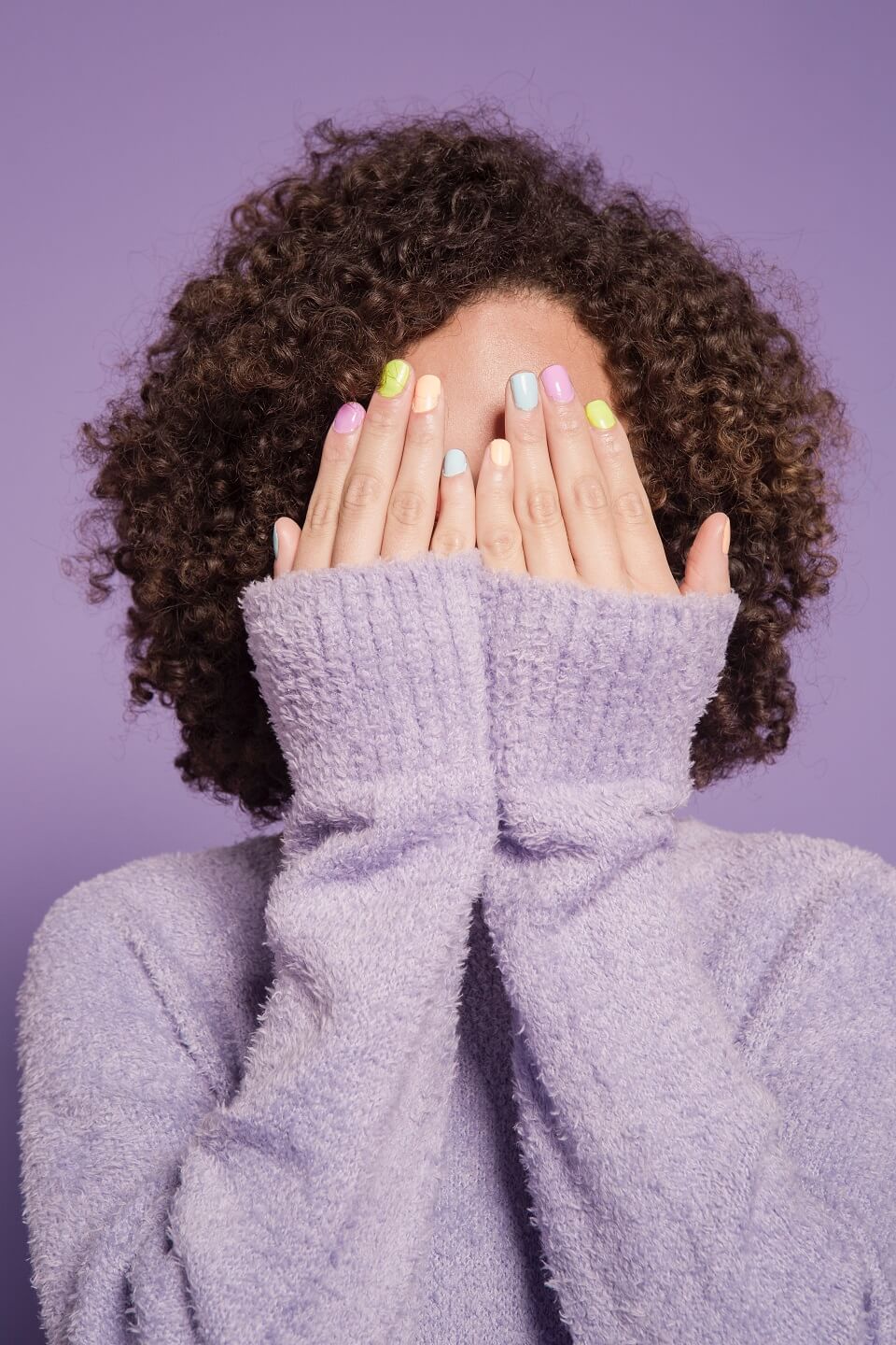 Black woman covering face with pastel nail polish on