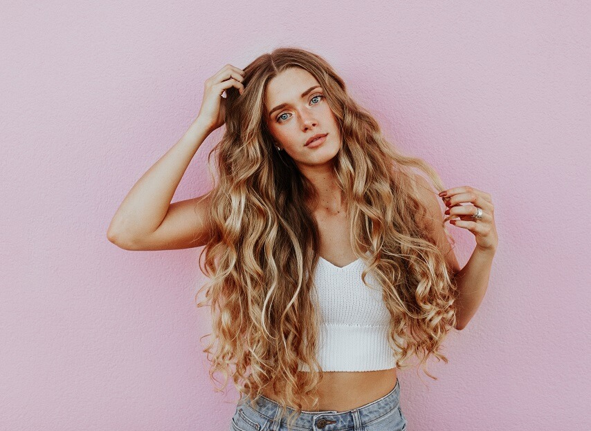 Woman with long, curly hair standing in front of a pink wall