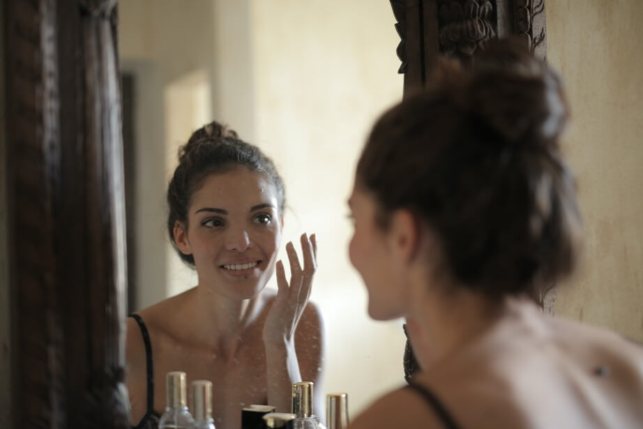 Woman reflected in a mirror applying skincare product