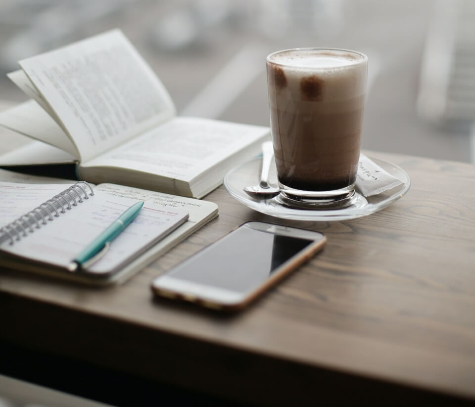 Coffee, phone, planner, and book on a table