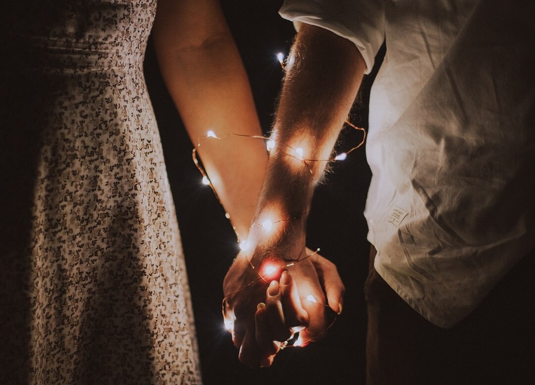 man and woman holding each others hand wrapped with string lights